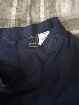 Mörkblå tights från Skins, storlek L - Säljer ett par mörkblå tights från Skins i storlek L. De har elastisk midja med logga och är gjorda i ett stretchigt syntetmaterial som sitter tight mot kroppen. Perfekta för träning och sport. Snyggt tryck med Skins på benet.