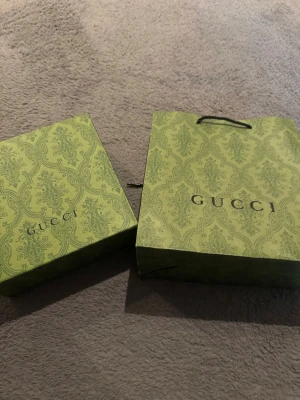 Grön shoppingväska - Säljer en snygg grön shoppingväskamed elegant mönster och klassisk logga på framsidan. Väskan har svarta handtag och är perfekt för dig som gillar lyxiga detaljer och stilren design.