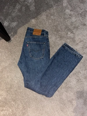 Levi's 501 jeans blå W30 L30 - Klassiska Levi's 501 jeans i blå denim med rak passform och fem fickor. Snyggt läderpatch bak i midjan och ikonisk röd Levi's-tag på bakfickan. Perfekt för dig som gillar tidlös stil och vill ha ett par jeans som funkar till allt.