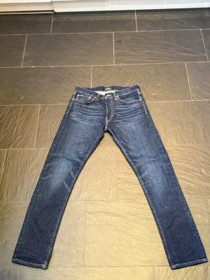 Mörkblå jeans från Polo Ralph Lauren - Snygga mörkblå jeans från Polo Ralph Lauren med klassisk femficksdesign och bruna detaljer på bakfickan. Jeansen har en rak passform och är tillverkade i slitstarkt bomullsmaterial. Perfekt för dig som gillar tidlös stil och vill ha ett par jeans som funkar till allt. orginal pris är 1799 och säljs för 699