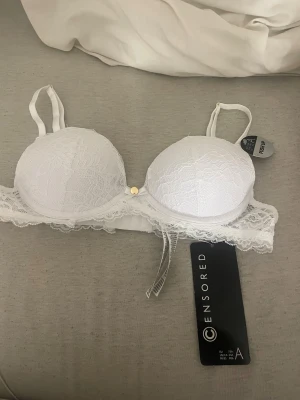 Vit spets push-up bh från new yorker  - Snygg vit push-up bh från new yorker i storlek 75A. Bh:n har vadderade kupor med spetsdetaljer och en liten rosett framtill. Axelbanden är justerbara och spetsen ger en extra feminin touch. Perfekt för dig som gillar stilrena underkläder med lite extra detaljer.