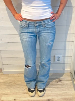 Levis 517 ljusblå bootcut jeans - Säljer ett par ljusblå Levis 517 jeans med bootcut passform och låg midja. Jeansen har slitna detaljer och hål vid knäna. Perfekt till skolan!💖