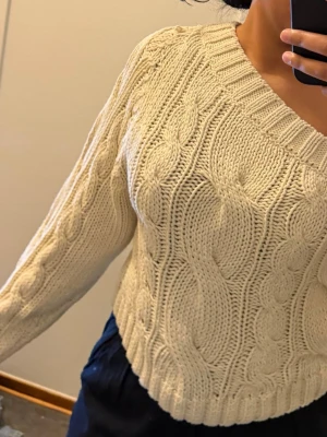 Beige stickad oneshouldertröja - Säljer en chunky beige stickad tröja med grovt kabelstickat mönster. Tröjan har en unik oneshoulder-design med bred ribbad kant och lång ärm. Perfekt för dig som vill ha något annorlunda och mysigt till hösten eller vintern.