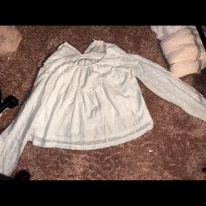 Ljusblå prickig blus från Gina Tricot - Supersöt ljusblå blus från Gina Tricot med diskreta vita prickar och långärmad design. Blusen har en lös passform och rundad halsringning, perfekt för en chill och stilren look. Tillverkad i mjukt bomullsmaterial.