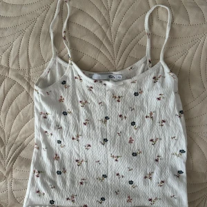 Vit blommig linnetopp XS - Supersöt vit linnetopp från 157 i storlek XS med små blommor i rosa och mörkblått. Tunt, krinklat tyg och smala axelband ger en chill och somrig vibe. Perfekt för varma dagar och enkel att matcha med jeans eller shorts.