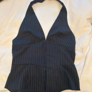 Svart randig halterneck topp - Snygg svart halterneck topp med vita tunna ränder och djup v-ringning. Toppen har figurnära passform. Perfekt för dig som vill ha en stilren och trendig look med lite edge. Helt ny