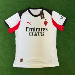 AC Milan fotbollströja puma 25/26  - AC Milan bortatröja i vitt med svarta och röda detaljer. Klassisk rund hals, kortärmad och tillverkad i lätt funktionsmaterial. Puma-logga på bröstet och ärmarna, klubbmärke och sponsortryck framtill. Perfekt för dig som vill visa ditt stöd på matchen.