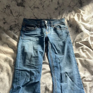Low waist, blå, bootcut jeans från Gina Young - Säljer ett par klassiska blå jeans från Gina Tricot Young  med utsvängda ben  och normal passform. Jeansen har fem fickor, dubbla knappar i midjan och snygga kontrastsömmar. De är i storlek 170 och jag säljer de för de satt för tajt. 