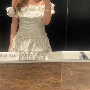 Vit offshoulder klänning med volang - Superfin vit kortklänning med offshoulder och volangdetaljer. Klänningen har broderade spetsmönster och är tillverkad i bomull. Perfekt för sommarens alla tillfällen, med romantisk och luftig känsla.