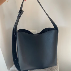 Svart axelväska med bred rem - Stilren svart axelväska i slätt skinn med bred, justerbar rem och magnetlås. Bra skick. 