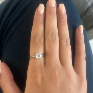 Äkta Silverring med stor glittrig sten - Snygg silverring med en stor, fyrkantig glittrig sten i mitten och små stenar längs bandet. Ringen har en elegant och modern design som verkligen drar blickarna till sig. Perfekt för dig som vill ha något som sticker ut och känns lyxigt.