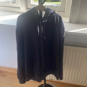 Mörkblå hoodie med dragkedja 157 - Mörkblå hoodie från 157 i storlek M. Tröjan har huva med snörning, hel dragkedja framtill och två stora fickor. Perfekt för chill dagar eller när du vill ha något bekvämt och stilrent. Materialet är mjukt och känns skönt mot huden.