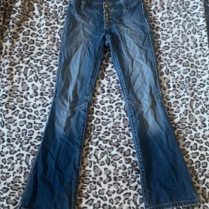 Lågmidjade bootcut jeans - Snygga blå bootcut jeans från Divided med låg midja och fem knappar framtill. 33cm midja. Tillverkade i klassiskt denimtyg. Slitna längst ner.