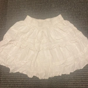 Vit volangkjol med resårmidja - Supersöt vit kortkjol med flera volanger och resår i midjan. Kjolen har en luftig och lätt känsla, perfekt för varma dagar. Den är enkel att matcha och ger en romantisk vibe till din outfit.