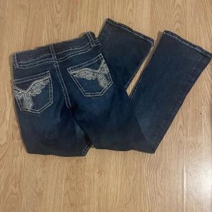 Mörkblå jeans med broderade fickor Gina Tricot - Mörkblå jeans från Gina Tricot med kontrastsömmar och snygga broderade bakfickor med paljettdetaljer. Klassisk femficksmodell med raka ben och låg midja. Perfekta för dig som gillar jeans med lite extra detaljer.