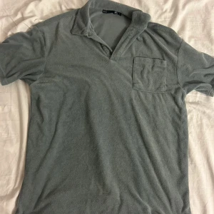 Grön piké tröja  - Grå t-shirt i mjuk frotté med klassisk krage och bröstficka. Perfekt för en chill och avslappnad stil. Kortärmad modell med relaxed fit och enkel design som funkar till det mesta.