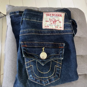 True Religion mörkblå bootcut jeans - Dem är low waist och utsvängda längst ner i modellen joey dem är i storlek w24/xs dem är inte mycket använda men dem har en liten slitning längst ner på ena benet men det syns inte alls. Säljer of dem är för långa, jag köpte dem för 1300kr säljer för 950 minst då dem ser nästan helt nya ut❤️