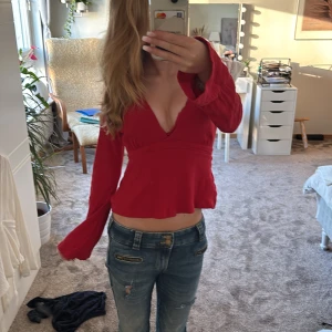 Röd omlottopp med v-ringning - Säljer en röd omlottopp med djup v-ringning och långa ärmar. Toppen har knytband i midjan och är tillverkad i ett lätt, strukturerat tyg som ger en snygg passform. Skulle säga att denna har krympt lite i tvätten som gör att den även kommer passa XSS. Såg precis det lilla hålet vid v-ringningen men absolut inget man märker. Pris kan diskuteras isåfall 💗