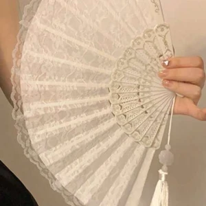 Vit spetsig solfjäder med tofs - Superfin solfjäder i vit spets med eleganta detaljer och en dekorativ tofs. Perfekt accessoar för att ge din look en vintagekänsla. Spetsmönstret gör den extra romantisk och stilren.