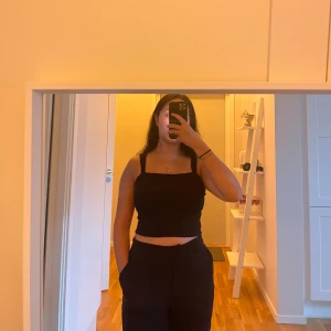 Svart croppad linnetopp - Säljer en svart croppad linnetopp med breda axelband och fyrkantig halsringning. Toppen är enkel och stilren, perfekt att matcha med höga byxor eller kjol. Materialet känns mjukt och lätt mot huden.