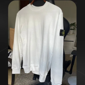 Vit Stone Island sweatshirt M - Vit sweatshirt från Stone Island med klassisk rund hals och långärmad passform. Tröjan har den ikoniska svarta patchen med gul och grön broderad logga på vänster ärm. Mjuk bomullskvalitet och normal passning storlek M. Har lappar kvar, inga tecken på användning.