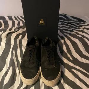 Svarta sneakers från Axel Arigato - Stilrena svarta sneakers från Axel Arigato i mocka med klassisk låg profil och vit platt sula. Skorna har snörning och diskret logga på sidan. Perfekta för dig som gillar minimalistisk och clean stil. Levereras med originalkartong och dustbag. Kommer tvättas innan säljning och priset är ej hugget i sten