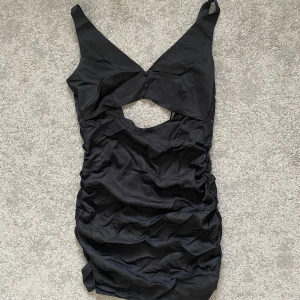 Svart omlott kortklänning med cut-out - Snygg svart kortklänning med omlott-design och en cool cut-out detalj framtill. Tyvärr är den för liten och har inte kommit till användning på länge🪩