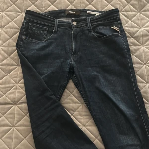 Replay Anbass jeans mörkblå 33/30 - Snygga Replay Anbass jeans i mörkblå tvätt med klassisk femficksdesign och raka ben. Jeansen har diskreta slitningar, logotyp på fickan och patch bak i midjan. Tillverkade i stretchig bomullsdenim för skön passform. Litet hål i skrevet men syns inte när jeansen sitter på.