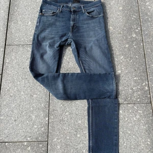 Blå jeans från Tiger of sweden - Snygga blå jeans från Tiger of Sweden med klassisk femficksdesign och raka ben. Jeansen har en mellanblå tvätt och detaljer i metall vid knappar och nitar. Perfekta för dig som gillar en enkel och stilren look. Storlek 34 men sitter tajtare 