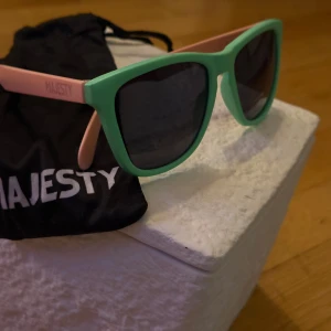 Mintgröna solglasögon från Majesty - Snygga solglasögon från Majesty med mintgrön front och ljusrosa skalmar. Modellen har en klassisk wayfarer-form och mörka linser som ger cool kontrast. Perfekt accessoar för att sticka ut och skydda ögonen mot solen.