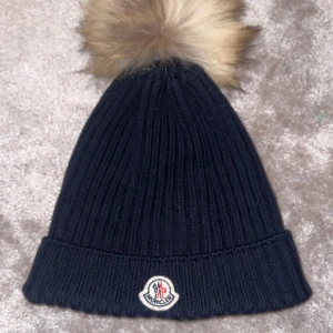 Mörkblå mössa från  Moncler - Snygg mörkblå ribbstickad mössa från Moncler med  beige pälsboll🩶