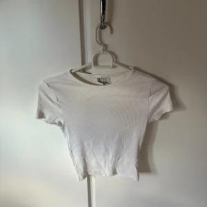 Vit ribbad topp från H&M Divided XS - En enkel och stilren vit ribbad topp från H&M Divided i storlek XS. Modellen är croppad med korta ärmar och rund halsringning. Perfekt att matcha med jeans eller kjol för en clean look.