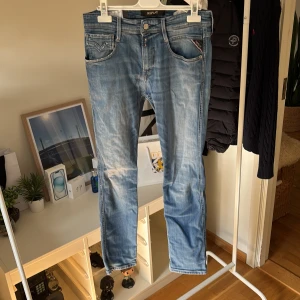 Blå jeans från Replay straight fit - Säljer ett par ljusblå jeans från Replay med klassisk femficksdesign och snygga slitningar. Jeansen har raka ben och normal passform, med detaljerade sömmar och logga på bakfickan. Perfekta för en avslappnad och stilren look. Storlek L30 W29