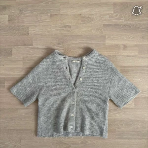 Grå stickad kofta - Supermjuk och ribbstickad grå kofta från Gina Tricot i kortare modell. Koftan har v-ringning, korta ärmar och knappar framtill. Perfekt att slänga över ett linne eller t-shirt för en chill look.