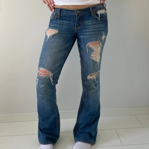 Blå bootcut jeans med slitningar - Snygga blå bootcut jeans från Hollister med rejält slitna detaljer och hål på både fram- och baksida. Jeansen har låg midja, klassiska fem fickor och är tillverkade i mjukt denim. Perfekta för dig som gillar en avslappnad stil.