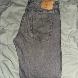 Grå jeans från Jack & Jones - Snygga grå jeans från Jack & Jones med klassisk femficksdesign och läderpatch bak i midjan. Jeansen har rak passform och är tillverkade i mjukt bomullsmaterial. Perfekta för dig som gillar en stilren och enkel look.