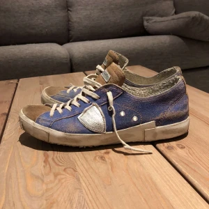 Philippe Model blå sneakers - Skriv förslag på pris. Säljer ett par Philippe Model sneakers i blå med bruna detaljer och silverfärgade inslag. Skorna har vit sula, snörning och rund tå. Klassisk streetstil med coola kontraster och logga under sulan. Perfekta för dig som gillar unika sneakers.