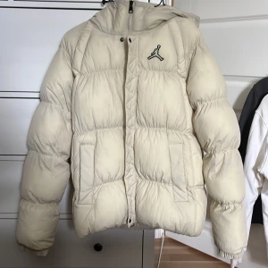 Jordan pufferjacka i beige med huva - Säljer en fet beige pufferjacka från Jordan med ikoniska Jumpman-loggan på bröstet. Jackan har stor huva, dragkedja och två fickor framtill. Perfekt för kalla dagar när du vill hålla stilen och vara varm. Oversized vibe och riktigt mjuk känsla. Storlek S men passar större. Köpt från JD sports. Nästan aldrig använd.