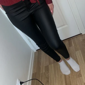 Svarta skinny byxor i skinnimitation - Säljer ett par svarta skinny byxor i skinnimitation med mellan midja. Byxorna har en tight passform och ger en snygg, glansig look. Perfekta för dig som vill ha en edgy stil och gillar att sticka ut.