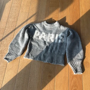Grå stickad tröja perfekt till hösten  - Grå stickad tröja med puffiga långärmar, varm och stockholmstil. Croppad modell med texten PARIS i vitt framtill. Perfekt till hösten 👌🏻💗