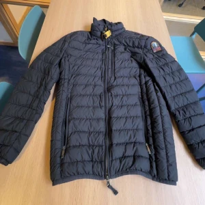 Svart dunjacka från Parajumpers - Snygg svart dunjacka från Parajumpers med klassisk patch på ärmen och gul detalj vid kragen. Perfekt för hösten 