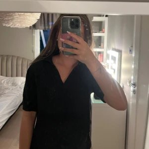 Svart t-shirt med krage och v-ringning - Snygg svart t-shirt med korta ärmar, krage och v-ringad hals. Perfekt för dig som gillar en enkel men stilren look. Materialet är handduksmaterial. Passformen är normal och t-shirten är lätt att matcha med dina favoritjeans eller kjol.