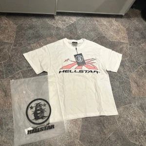 Vit Hellstar t-shirt med tryck - Säljer en vit t-shirt från Hellstar med stort grafiskt tryck i svart och rosa både fram och bak. T-shirten har rund hals och korta ärmar. Materialet är mjuk bomull och passformen är normal. Perfekt för dig som gillar streetwear vibes.