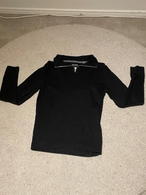Svart half zip tröja från Jack & Jones - Säljer en svart långärmad tröja från Jack & Jones med half zip-dragkedja i silver vid kragen. Tröjan har en stilren och enkel design med ribbad nederkant och är tillverkad i ett mjukt stickat material. Perfekt för dig som gillar klassiska och snygga plagg.