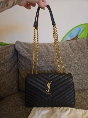 Svart quiltad axelväska från Saint Laurent - Säljer en svart quiltad axelväska från Saint Laurent med guldiga kedjor och YSL-logga framtill. Väskan är tillverkad i skinn och har flera fack med dragkedja inuti. Perfekt storlek för det viktigaste och riktigt snygg design. Dustbag & kartong ingår vid köp. 