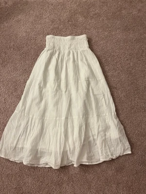Vit långkjol med volang - Säljer en vit långkjol med bred smock i midjan och flera volanger. Super gullig. Strl 152