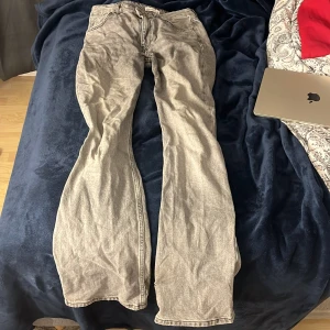 Grå bootcut jeans från Gina Tricot  - Säljer ett par gråa bootcut jeans från Gina i storlek 38. Jeansen har klassisk femficksdesign, slitna kanter längst ner på benen. Materialet är robust denim och färgen är ljusgrå med tvättad look.