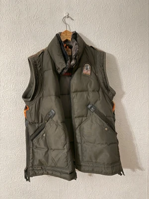 Mörkgrön dunväst från Parajumpers - Säljer en ÄKTA mörkgrön dunväst från Parajumpers med hög krage och coolt märke på bröstet. Västen har två stora fickor med dragkedja och snygga detaljer i svart. Perfekt för lager-på-lager och outdoor-vibe.