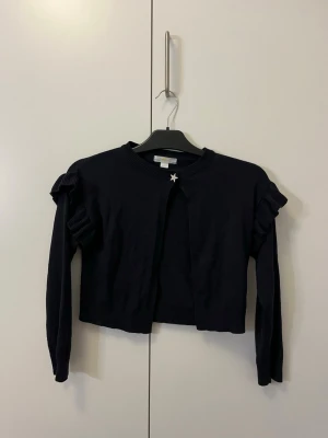 Marinblå kofta från Gina tricot (Young) 134/140 - Säljer en marinblå kofta från Gina tricot med långa ärmar och volangdetaljer på axlarna. 