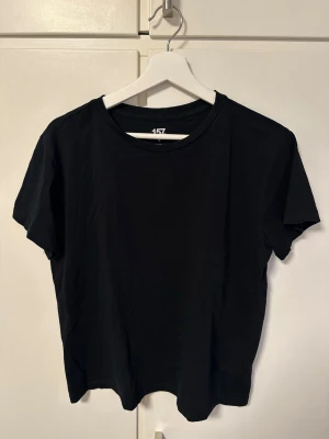 Svart t-shirt Lager 157 - En basic svart t-shirt från Lager 157 i storlek M. Tillverkad i 100% bomull med klassisk rund halsringning och korta ärmar. 
